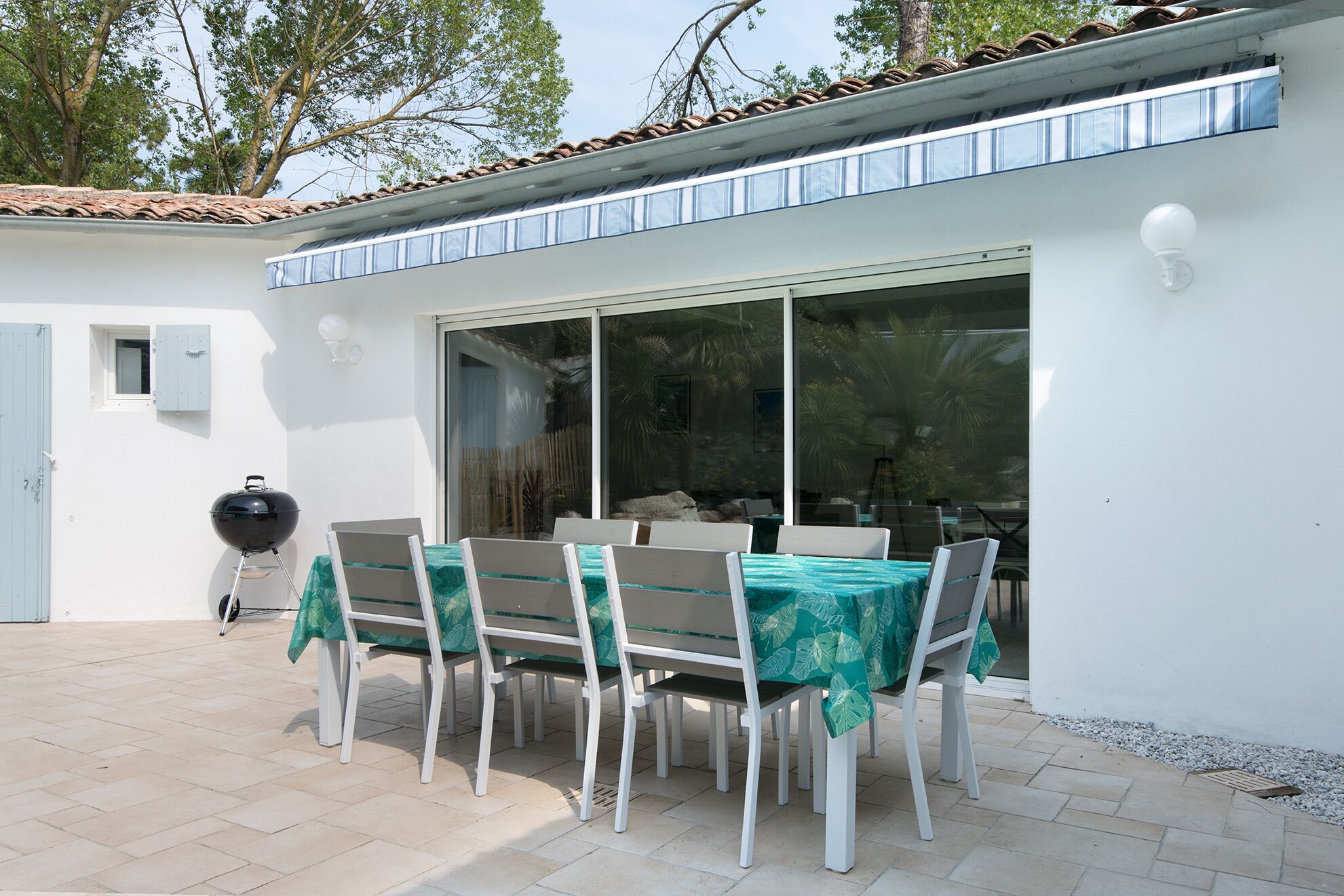 Un patio al aire libre con mesa y sillas, una parrilla y una puerta corrediza de vidrio que da a una zona cubierta.
