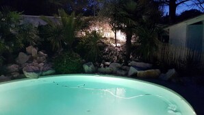 A swimming pool surrounded by rocks and plants, with a building in the background.