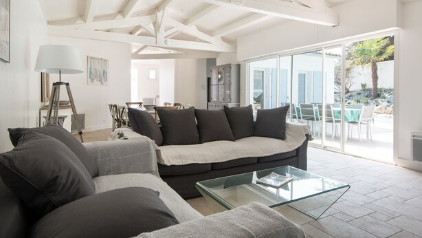 A modern living room with a sofa, a glass coffee table, and a dining area with chairs and a table.