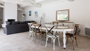 A modern living room with a dark grey sofa, a dining table with white chairs, and a large mirror above the table.
