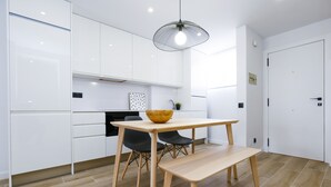 A modern kitchen with white cabinets, a wooden dining table, and a black pendant light. - SOL DE ESPAÑA Apartments - Beachfront (Cambrils)