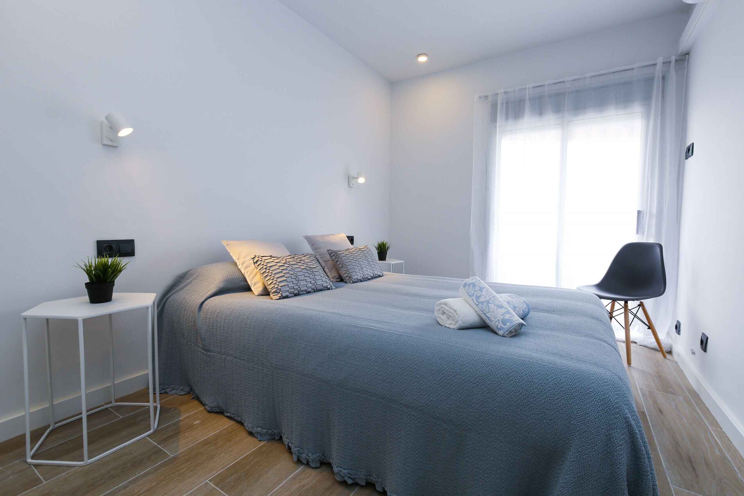 Una camera da letto moderna con un letto rifatto, un tavolino con una pianta e una sedia vicino alla finestra.