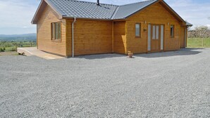A wooden cabin with a gravel driveway, a chimney, and a view of the landscape.