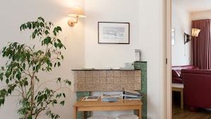A room with a wooden table, two white stools, a potted plant, a bulletin board, and a framed picture on the wall.