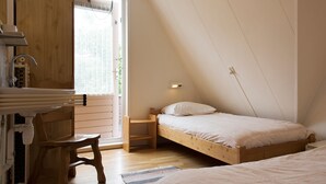 A small, cozy bedroom with a sloped ceiling, a wooden bed, a nightstand, a chair, and a window with a view of greenery outside.