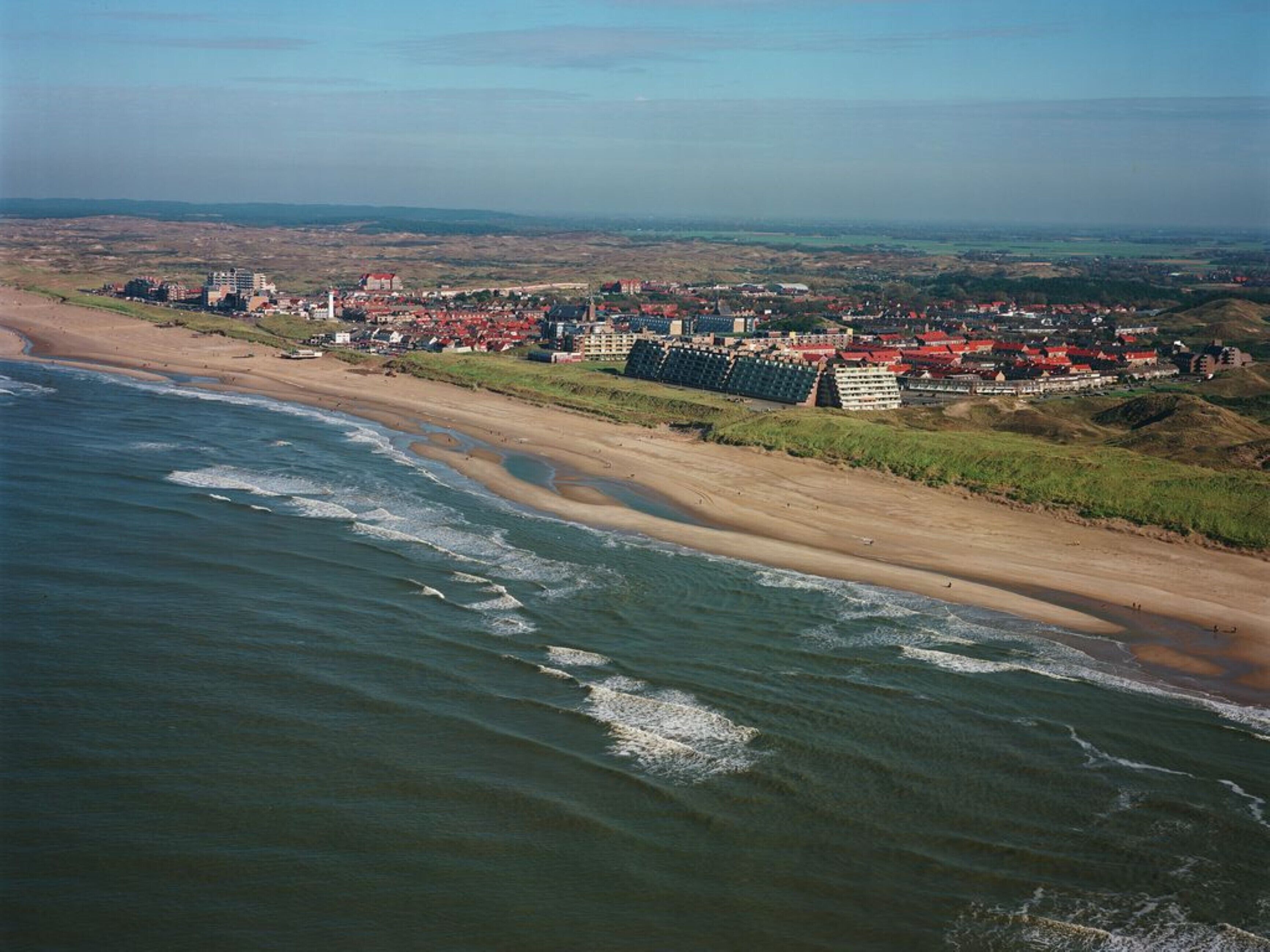 A coastal town with a beach, buildings, and a hilly landscape in the background.