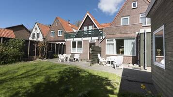 Een woonhuis met een verzorgd gazon, een terras met tuinmeubilair en een huis met een bakstenen gevel en pannendak.