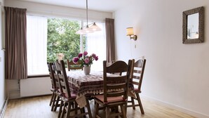 A dining area with a wooden table, chairs, a vase of flowers, and a window with curtains.