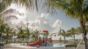 A playground with a red slide and water play area, surrounded by palm trees and benches. - Hemingway Hideaway in the Truman Annex (Key West)