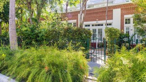 A building with a brick facade, numbered 21, surrounded by lush greenery and a green gate. - Hemingway Hideaway in the Truman Annex (Key West)
