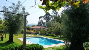 A swimming pool surrounded by lush greenery and a stone building with a red roof. - Solar das Bouças (Amares)