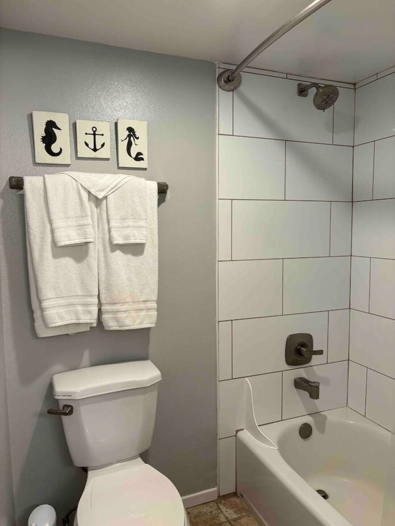 A bathroom with a toilet, two towels, a shower, and three wall-mounted signs.