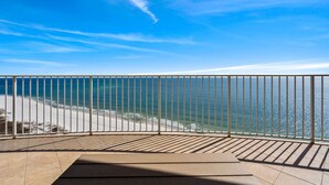 En balkon med gelænder i metal, udsigt over en strand og havet.