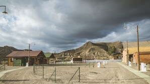 A fenced area with a building that has a green roof and a wooden exterior. - Camping Fort Bravo (Tabernas)
