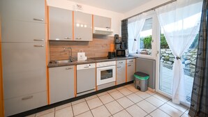 A modern kitchen with grey cabinets, a built-in oven, a coffee machine, and a window with curtains.