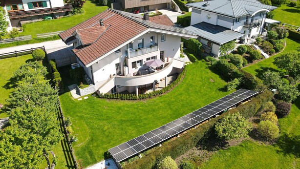A modern house with a large garden, solar panels, and a swimming pool.