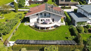 A large house with a curved balcony, surrounded by a well-maintained lawn and a solar panel array.