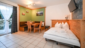A room with a bed, a table with chairs, a bench, and a TV mounted on the wall.