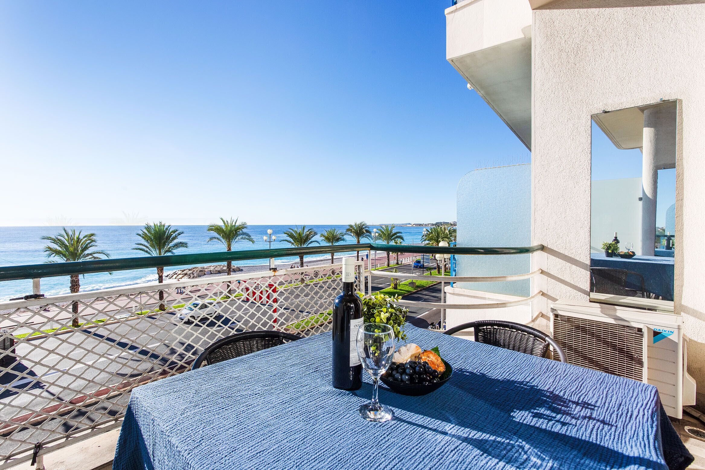 Ein Tisch mit einer Weinflasche, einem Glas und einem Teller Essen auf einem Balkon mit Blick auf das Meer.