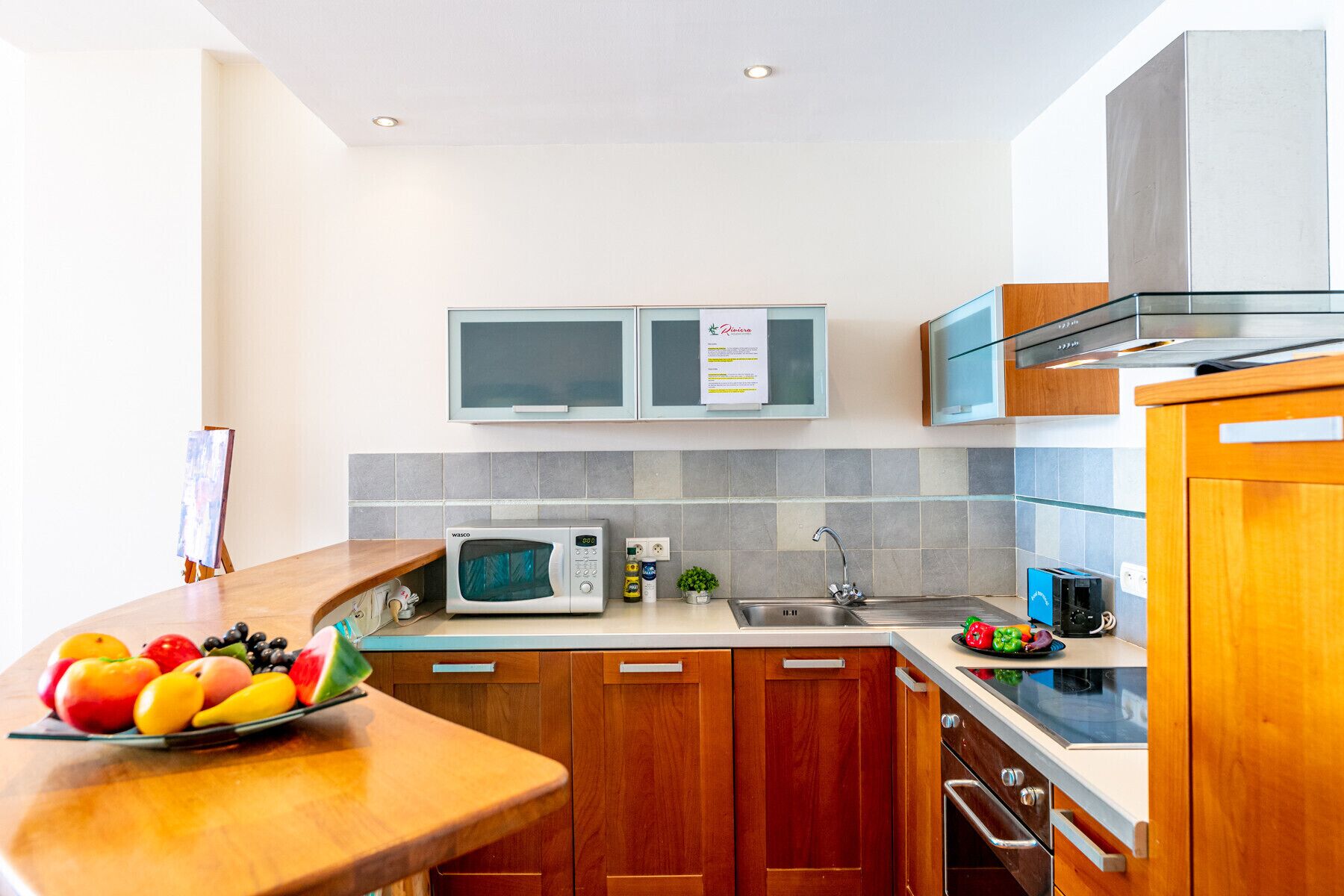 A modern kitchen with wooden cabinets, a microwave, a sink, and a fruit bowl on the counter.
