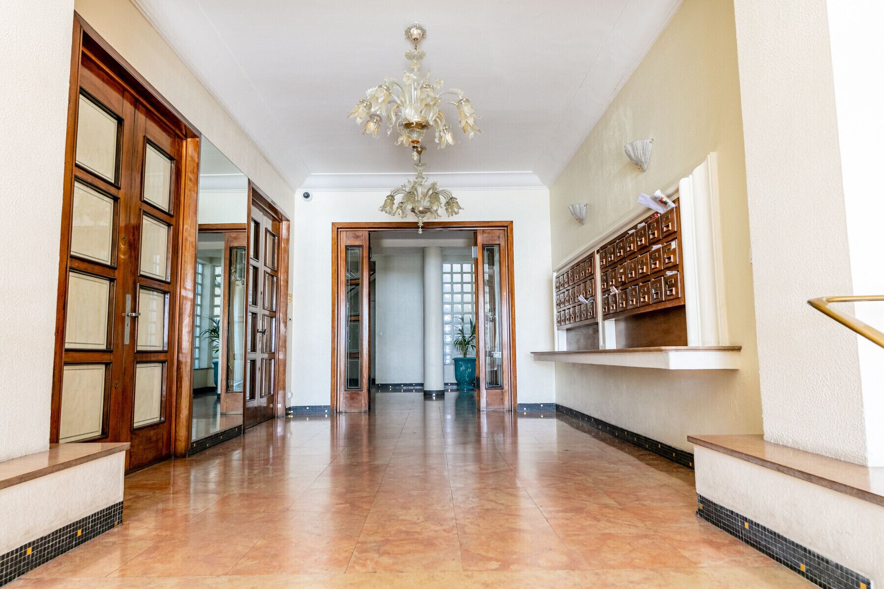 A spacious hallway with a polished floor, a chandelier, and a wall-mounted shelf with storage boxes.