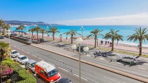 A coastal road with a view of the beach, palm trees, and parked cars.