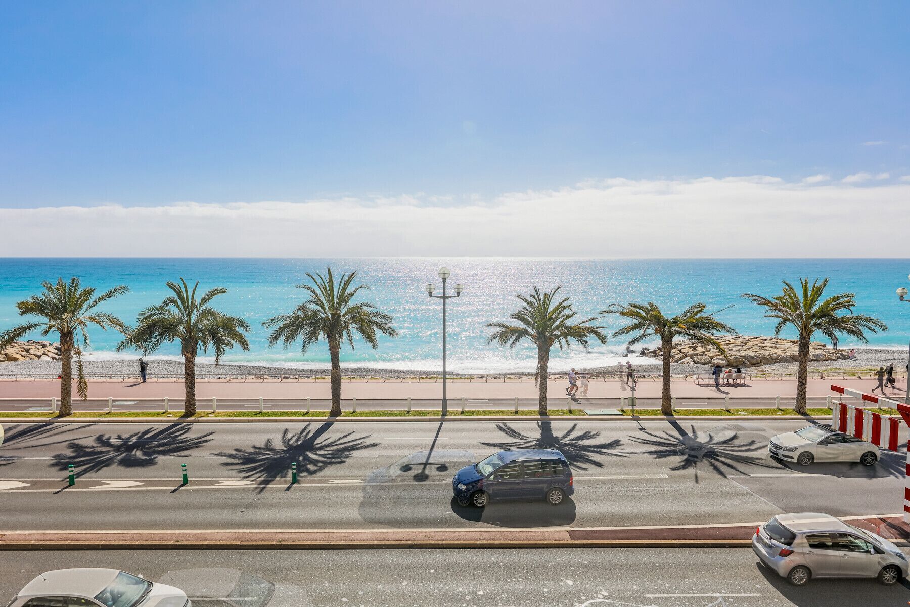 A coastal road with palm trees, a beach, and a clear blue sky.