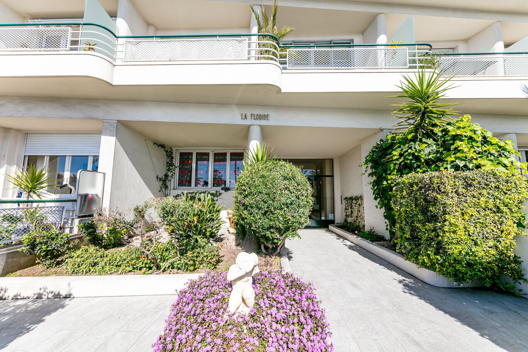 A hotel entrance with a covered walkway, a statue, and various plants.