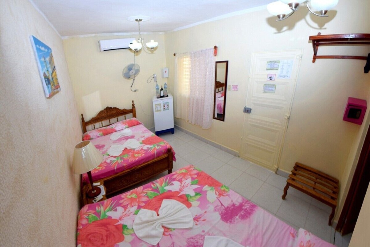 A bedroom with two beds, a bedside table, a mirror, a wardrobe, and a small wooden bench.