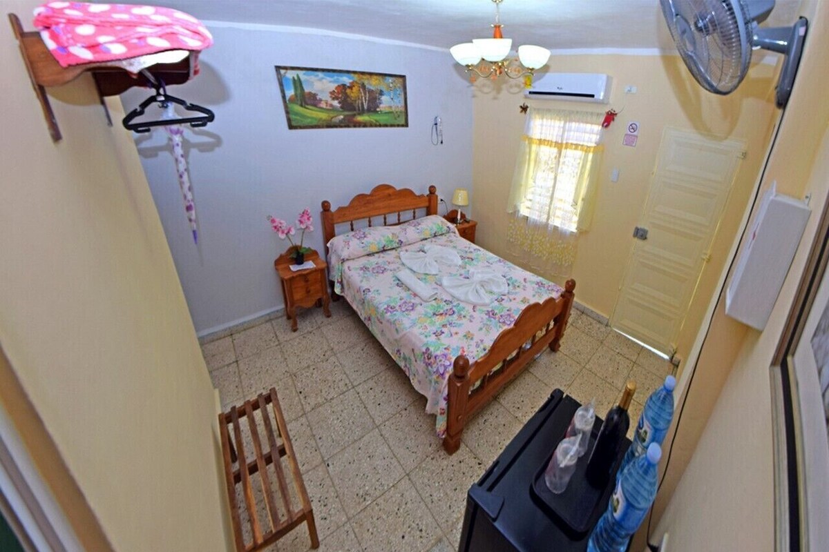A bedroom with a bed, a bedside table, a hanging chair, a water dispenser, and a window with curtains.