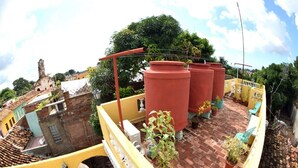 A rooftop terrace with terracotta pots, potted plants, and a yellow railing. - Hostal Casa Azul Santa Ana TRINIDAD (Trinidad)