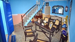 A room with a staircase, wooden furniture, a fan, and a 'BIENVENIDO' sign. - Hostal Casa Azul Santa Ana TRINIDAD (Trinidad)