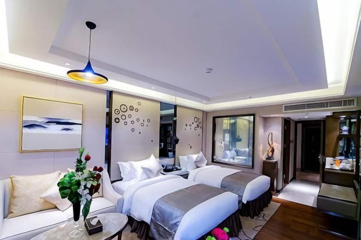 A modern hotel room with two beds, a sofa, a dining table, and a large window.