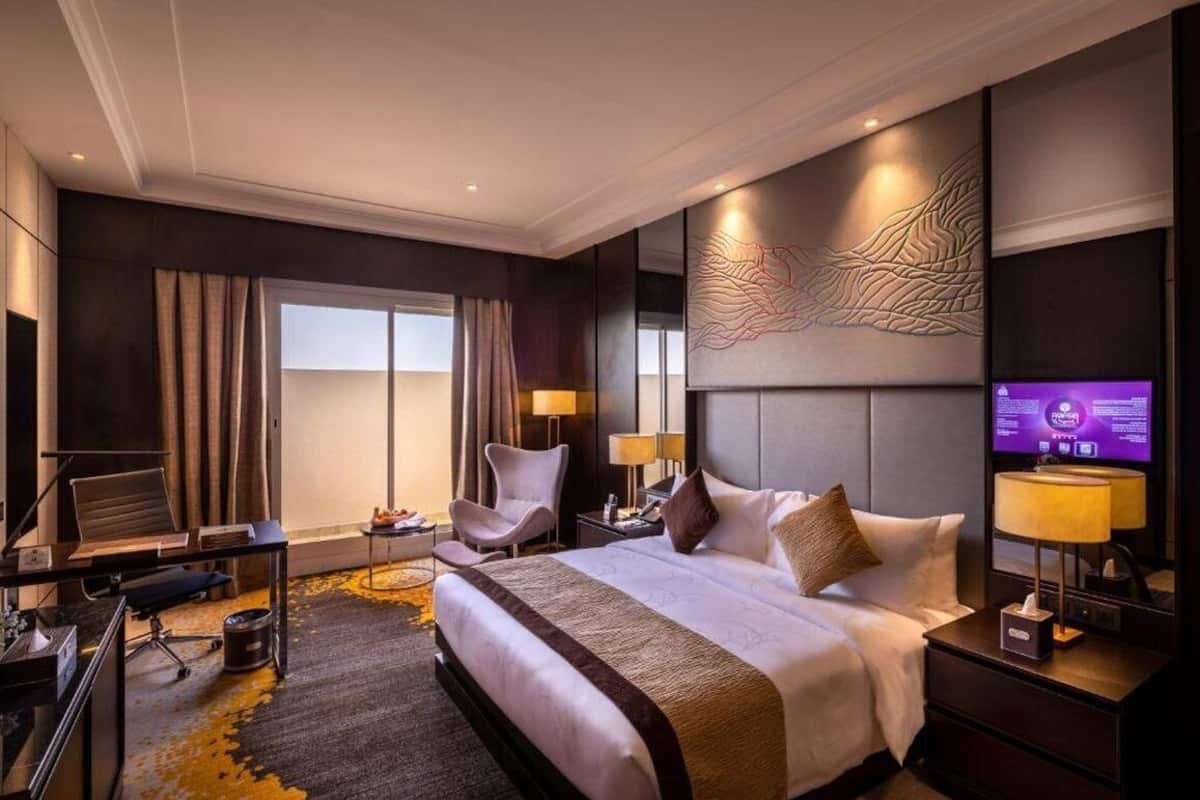 A modern hotel room with a large bed, a desk, a chair, and a television.