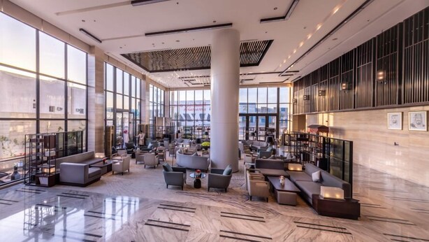 Een ruime lobby met een hoge plafond, grote ramen en moderne zitopstellingen.