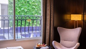 Een moderne hotelkamer met een groot raam, een ronde tafel met een schaal fruit, een comfortabele fauteuil en een klein nachtkastje.