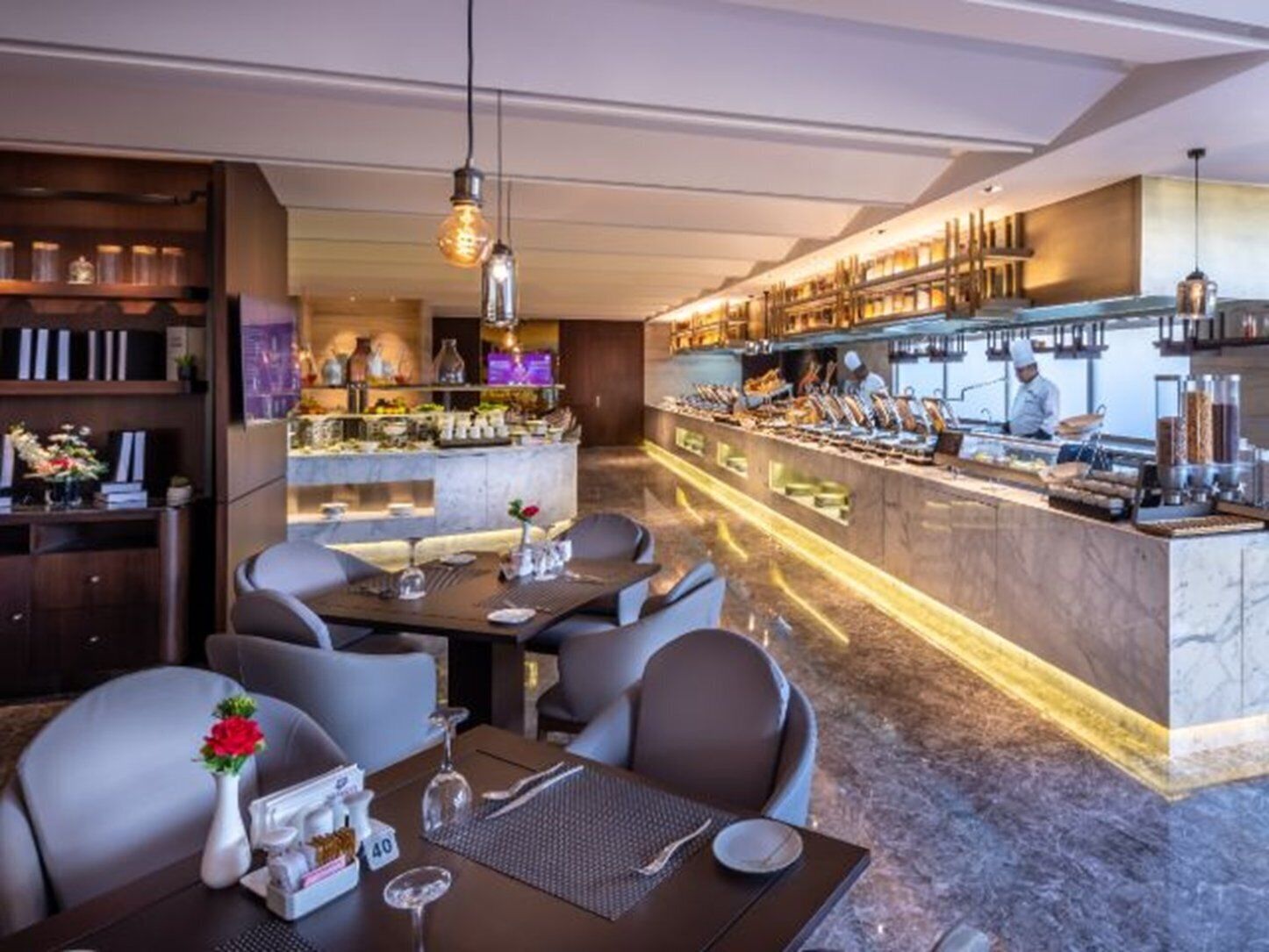 A modern restaurant with a bar area, marble flooring, and a chef preparing food.