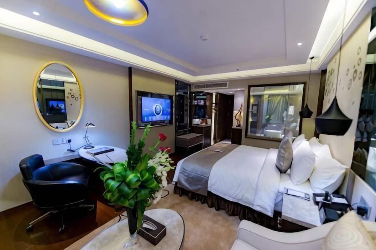 A modern hotel room with a bed, desk, chair, TV, and a large mirror.