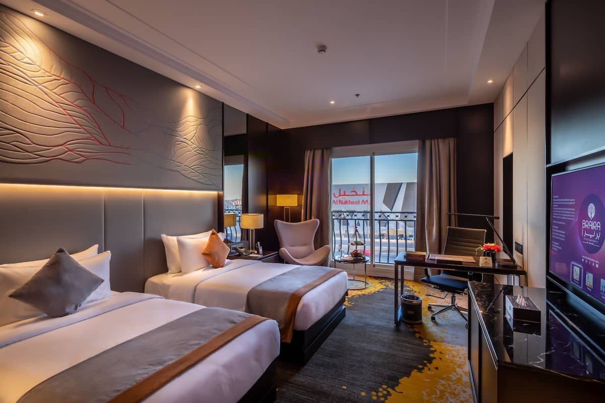 A hotel room with two beds, a desk, a chair, a TV, and a balcony with a view.