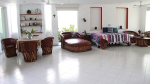 Een ruime kamer met een groot bed, een eettafel met stoelen, een bank en een kleine tafel met een vaas.
