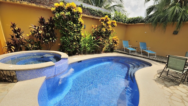 Una piscina con borde de azulejos, rodeada de plantas y sillas.