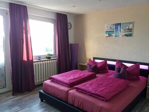A bedroom with a bed, curtains, a radiator, a wall clock, and a window. - dog-friendly vacation home - vacation home (Kröslin)
