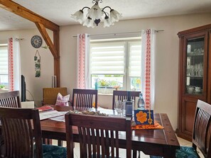 A dining area with a wooden table, chairs, a chandelier, and a window with curtains. - dog-friendly vacation home - vacation home (Kröslin)