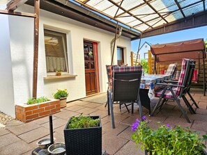 Um pátio externo com mesa, cadeiras, área coberta e plantas em vasos.