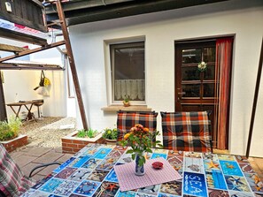 A patio with a table covered in a mosaic of sea-themed tiles, two plaid chairs, a vase with flowers, and a wooden ladder leaning against a white wall. - dog-friendly vacation home - vacation home (Kröslin)
