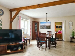 A dining area with wooden chairs, a table, a TV, and a window with curtains. - dog-friendly vacation home - vacation home (Kröslin)