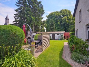 Um jardim bem cuidado com área de churrasco, cerca de madeira e um caminho que leva a um edifício.