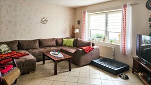 Un salon avec un canapé, une table basse, un téléviseur et une fenêtre avec des rideaux.