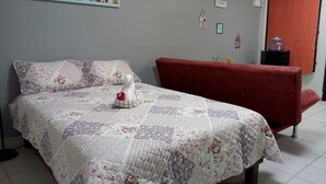 A bedroom with a floral quilted bedspread, a red sofa, and a wall with a painting of animals.