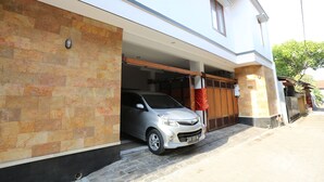 Ein silbernes Auto steht in einer Garage, die an ein modernes Haus mit Steinverkleidung und einer Holztür angebaut ist.